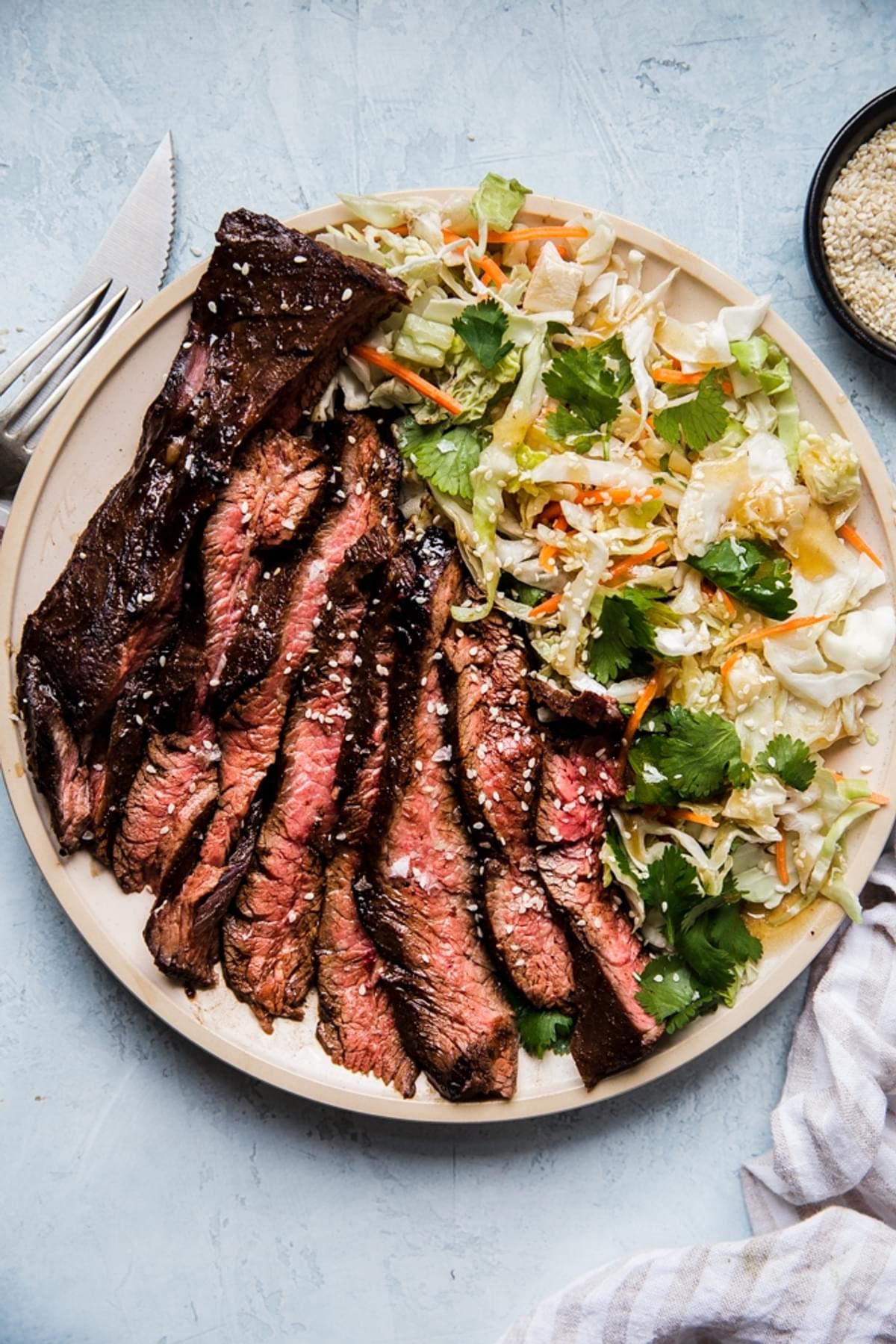 thin slices of grilled flank steak marinated in hoisin and five spice next to an asian salad on a plate