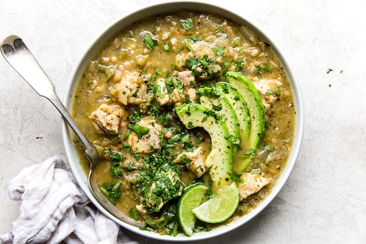 a bowl of homemade green chicken chili soup topped with avocado, cilantro and lime wedges