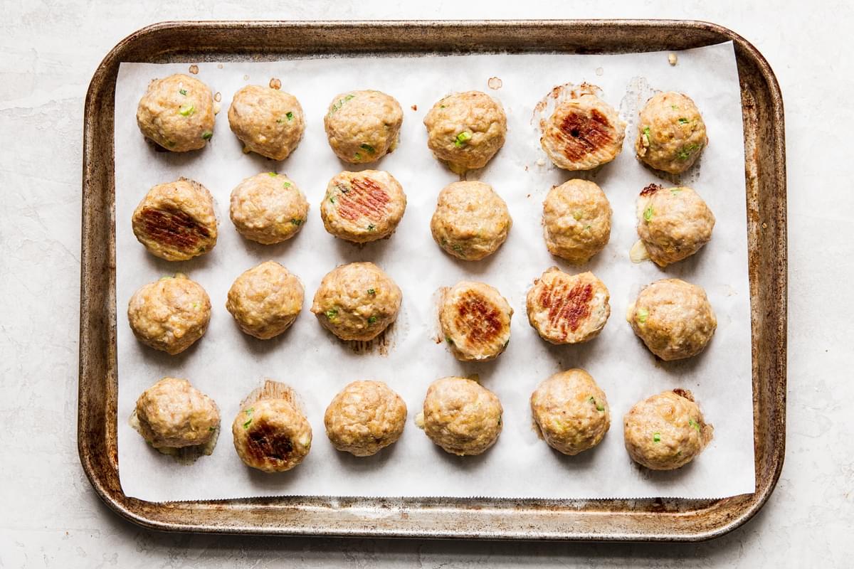 baked chicken meatballs on a parchment paper lined baking sheet