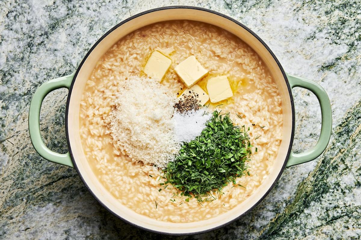 butter, parmesan, fresh herbs, salt and pepper being added to a pot of risotto