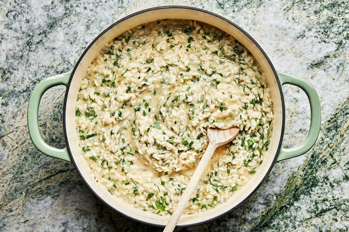 homemade fresh herb risotto made with butter, parmesan, garlic, shallots and lemon in a pot with a wooden spoon