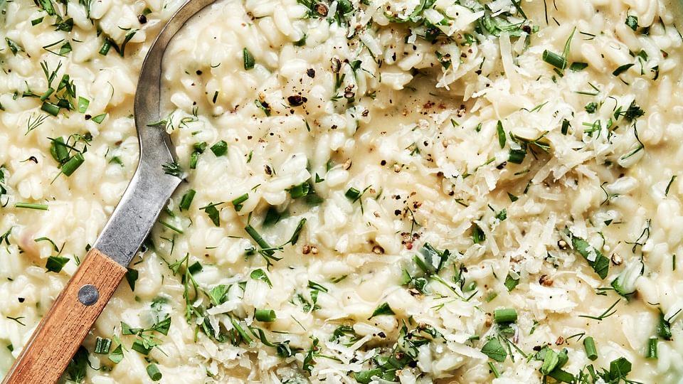homemade herb risotto in a bowl with a serving spoon made with butter, parmesan and lemon