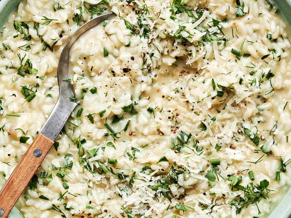 homemade herb risotto in a bowl with a serving spoon made with butter, parmesan and lemon