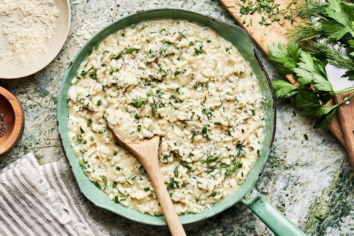 homemade fresh herb risotto made with butter, parmesan, garlic, shallots and lemon in a pot with a wooden spoon