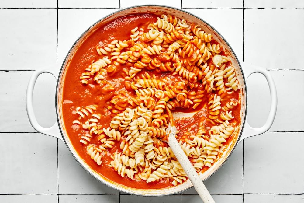 fussili pasta being tossed with spicy tomato sauce in a pot