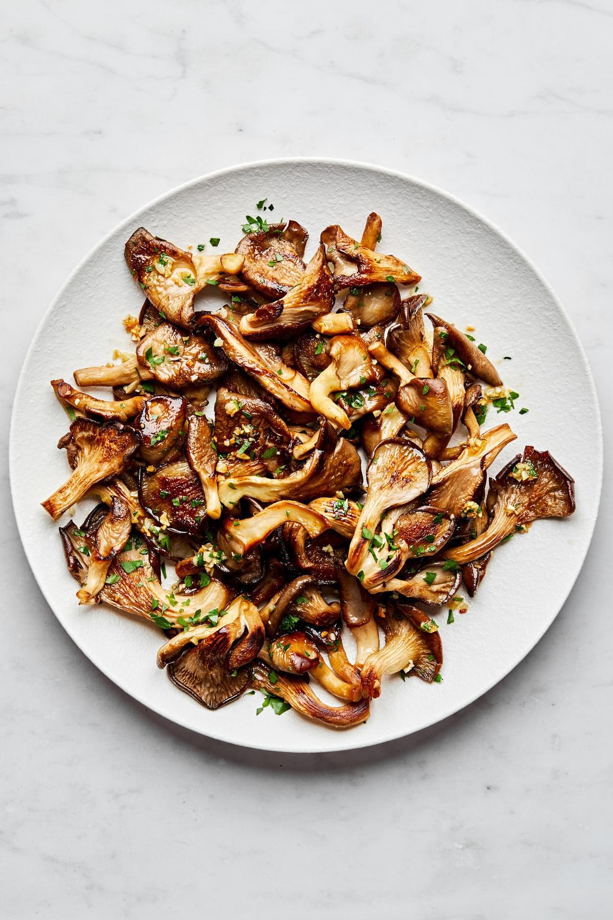 a plate of garlic butter oyster mushrooms cooked in salt, olive oil, butter, garlic and sprinkled with fresh parsley