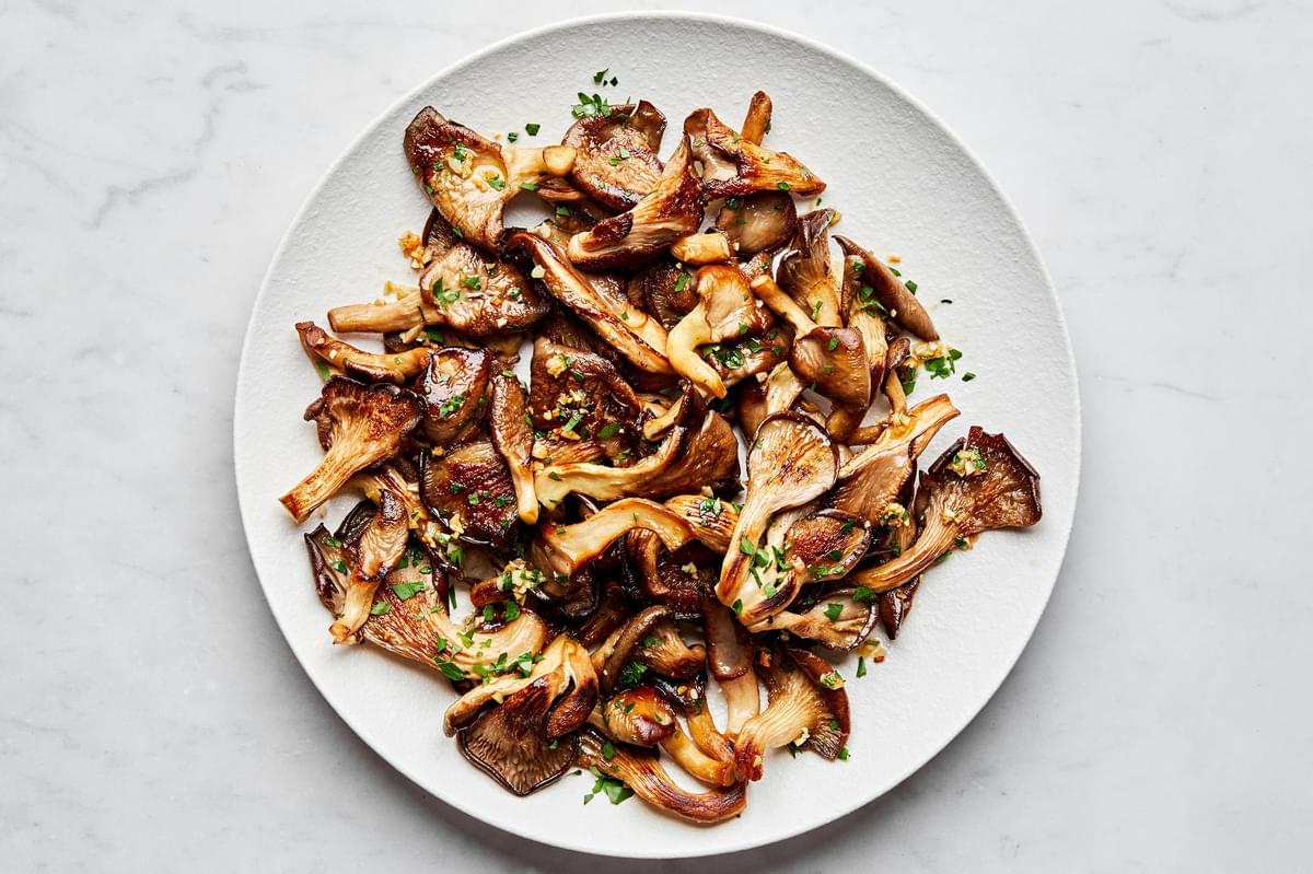 a plate of garlic butter oyster mushrooms cooked in salt, olive oil, butter, garlic and sprinkled with fresh parsley