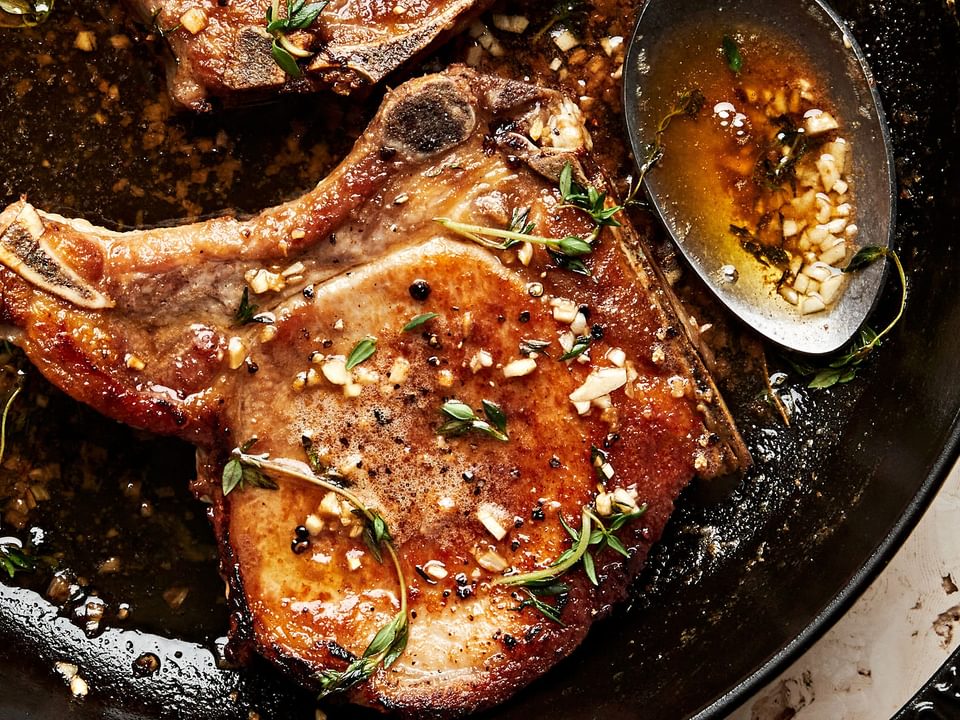 garlic butter pork chops in a skillet with melted herb butter being spooned over the top