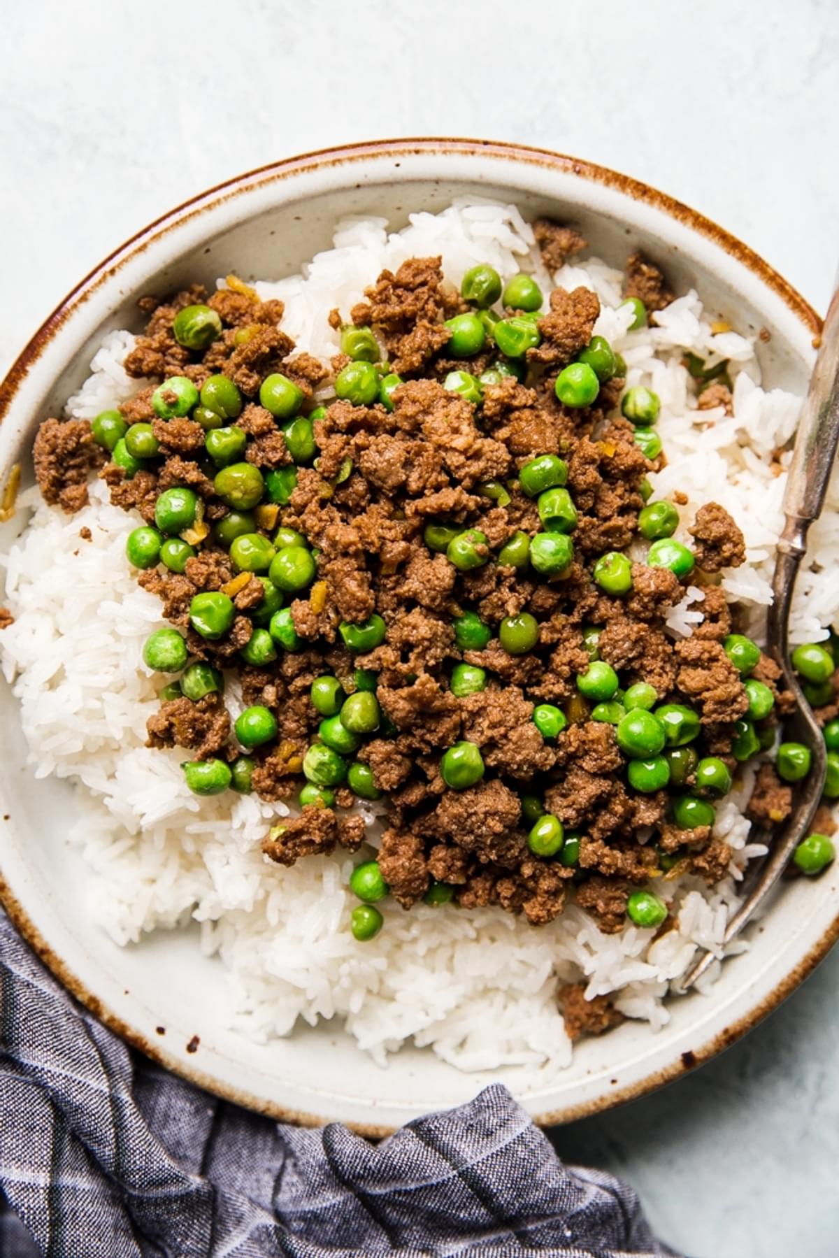 Japanese ginger beef on a plate with peas over rice with a fork