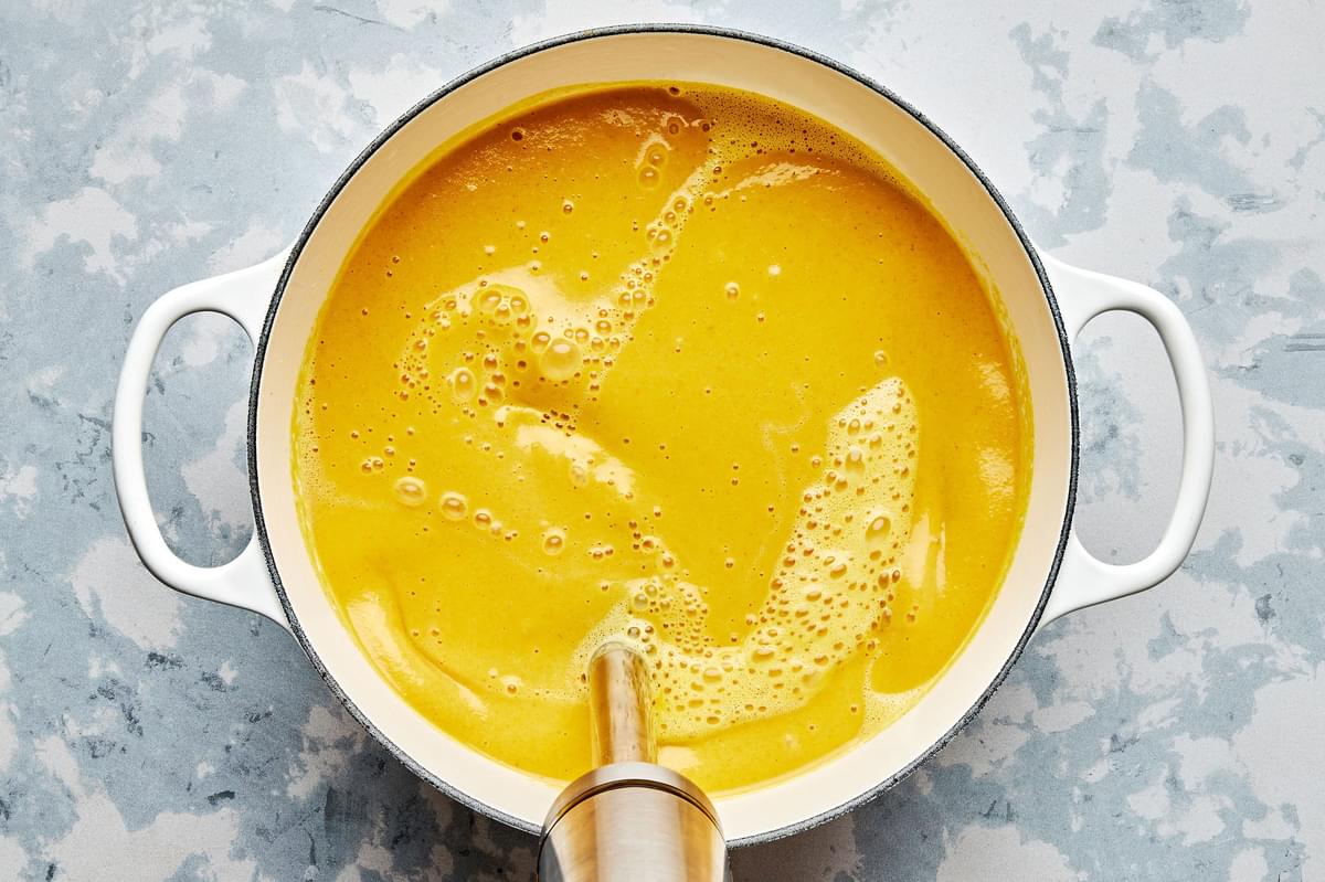 homemade golden soup being mixed with an immersion blender in a large pot