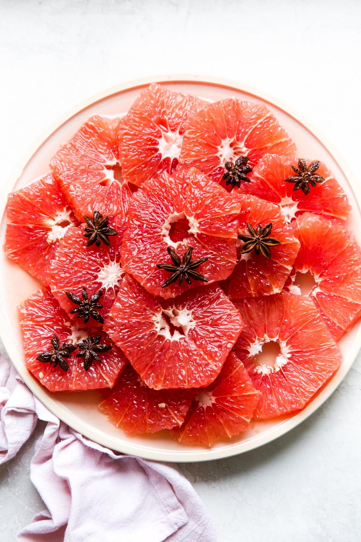 slices of red grapefruit on a plate with star anise simple syrup