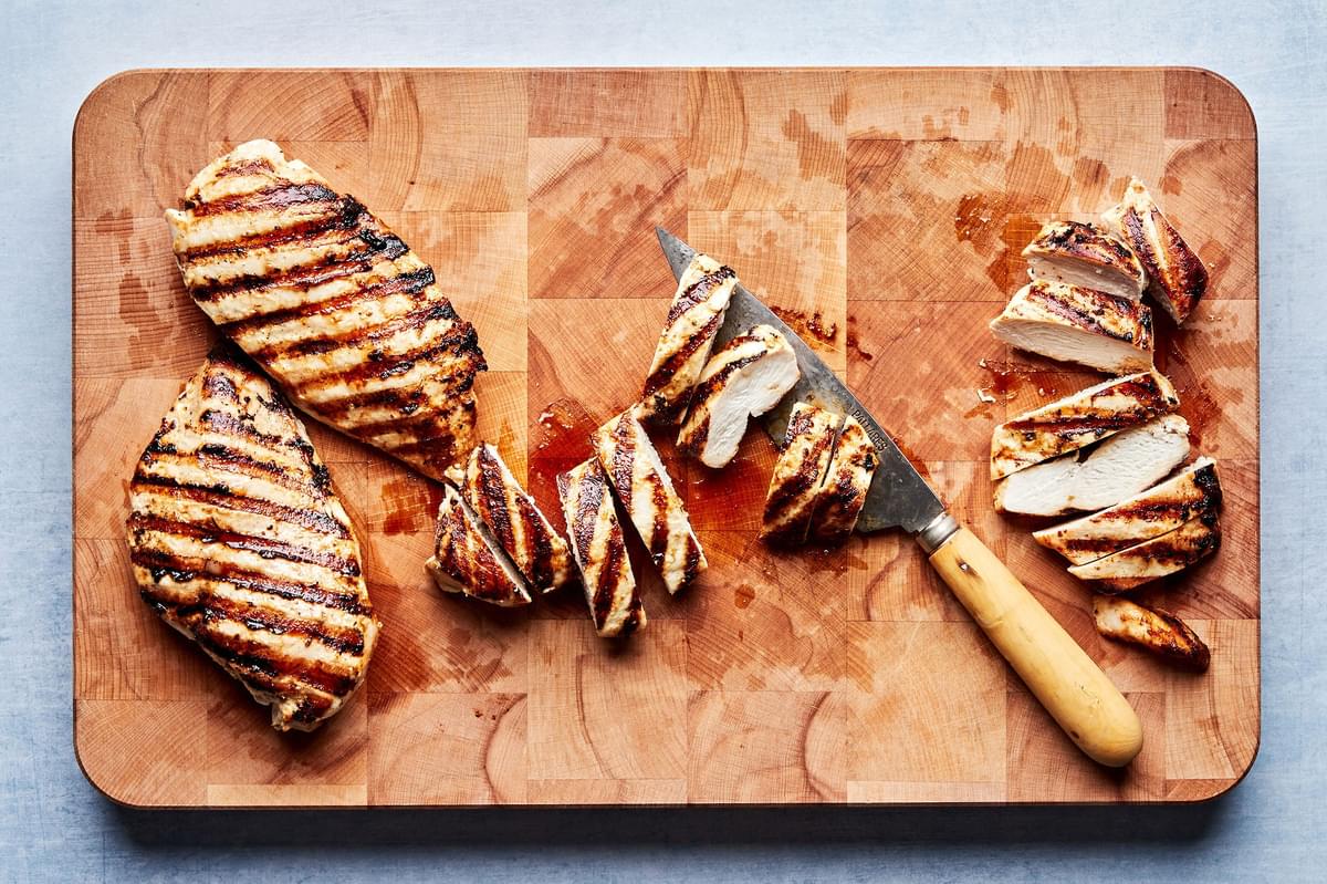 greek grilled chicken being sliced on a cutting board with a knife