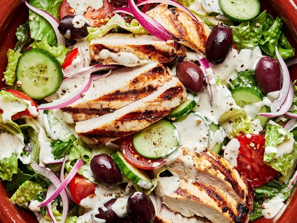 Greek Grilled chicken with salad topped with cucumbers, tomatoes cucumbers, sliced  Kalamata olives and red onion