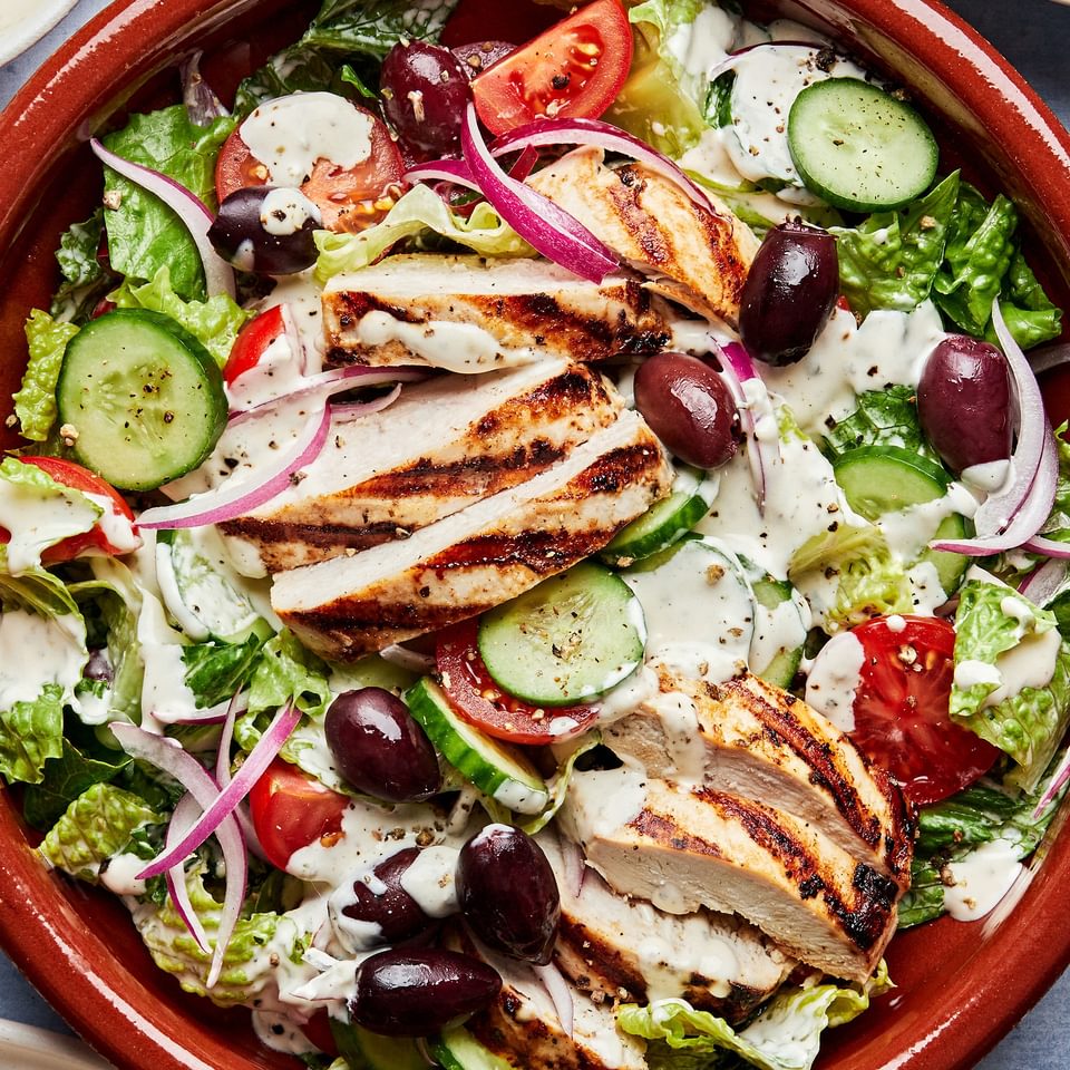 Greek Grilled chicken with salad topped with cucumbers, tomatoes cucumbers, sliced  Kalamata olives and red onion