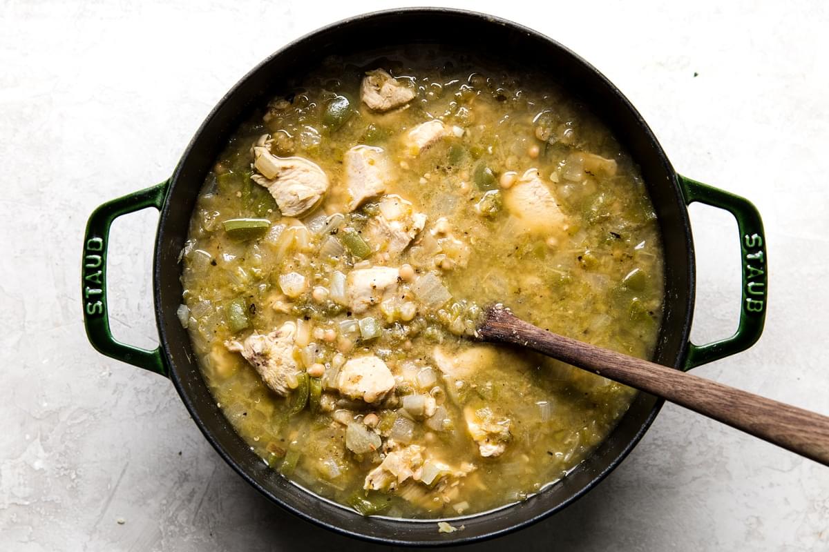cooked Green Chicken Chili Soup being stirred with a wooden spoon in a stock pot