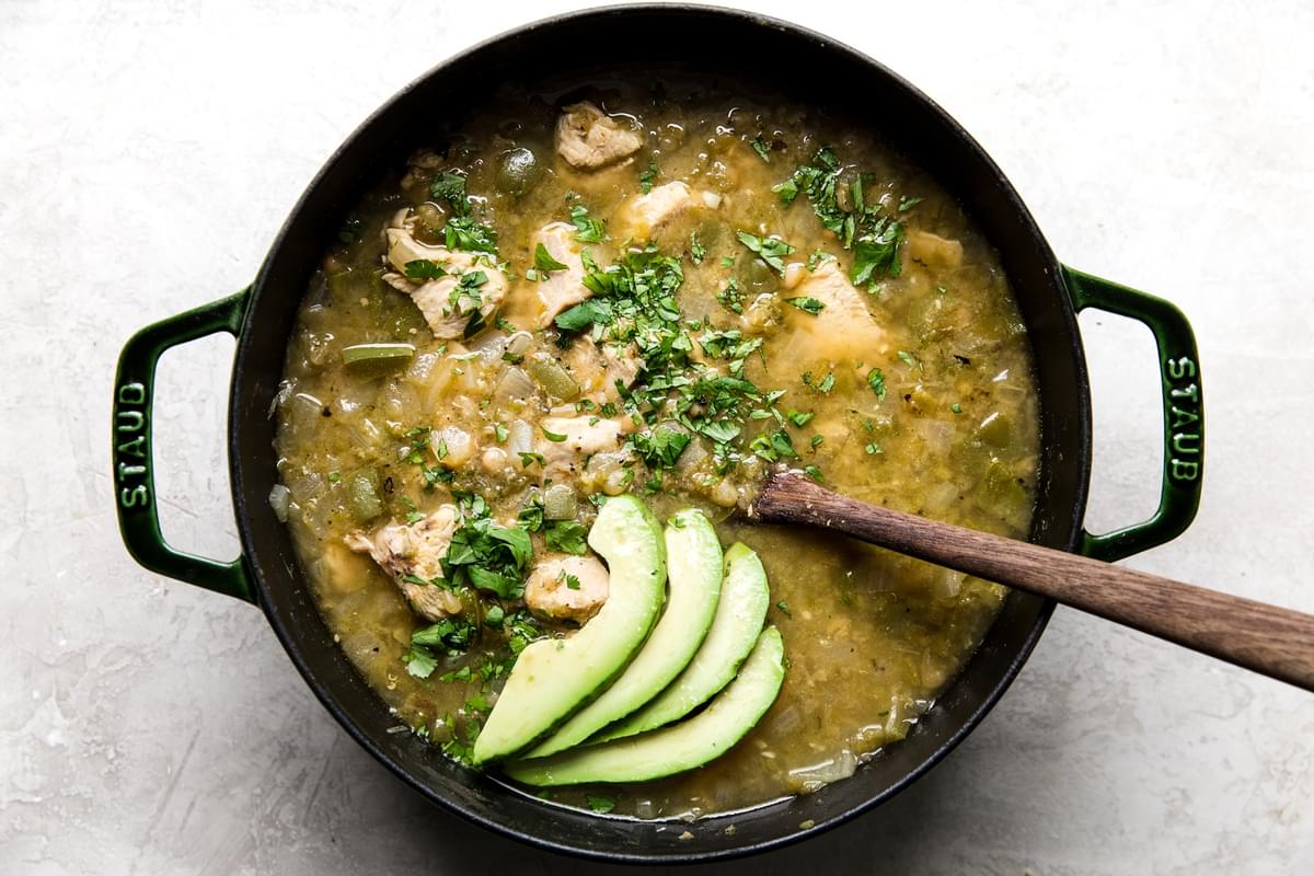 a pot of homemade Green Chicken Chili Soup topped with avocado and cilantro