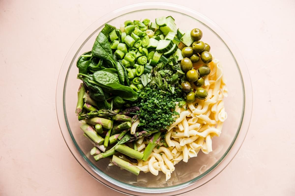 cooked pasta, olives, asparagus, spinach, green onions, in a glass bowl