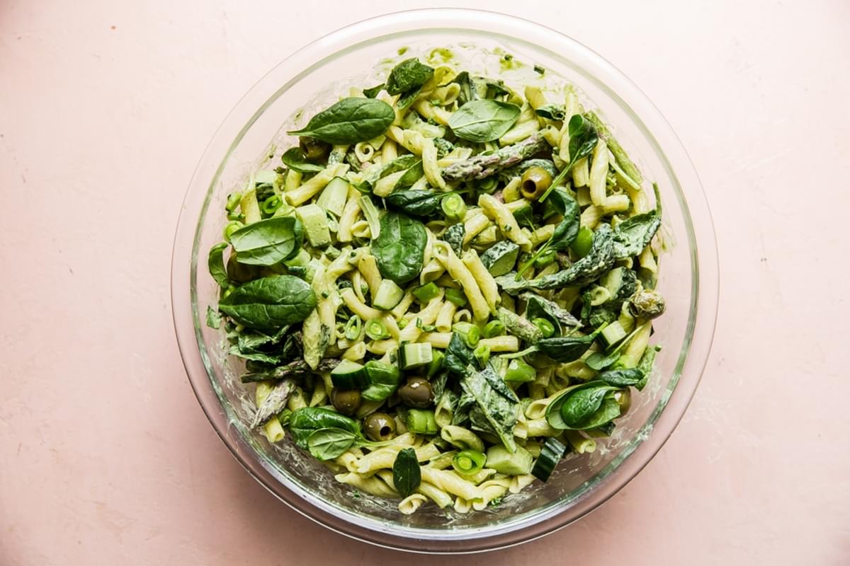 green goddess pasta salad in a glass bowl with olives, asparagus, spinach, green onions, in a glass bowl