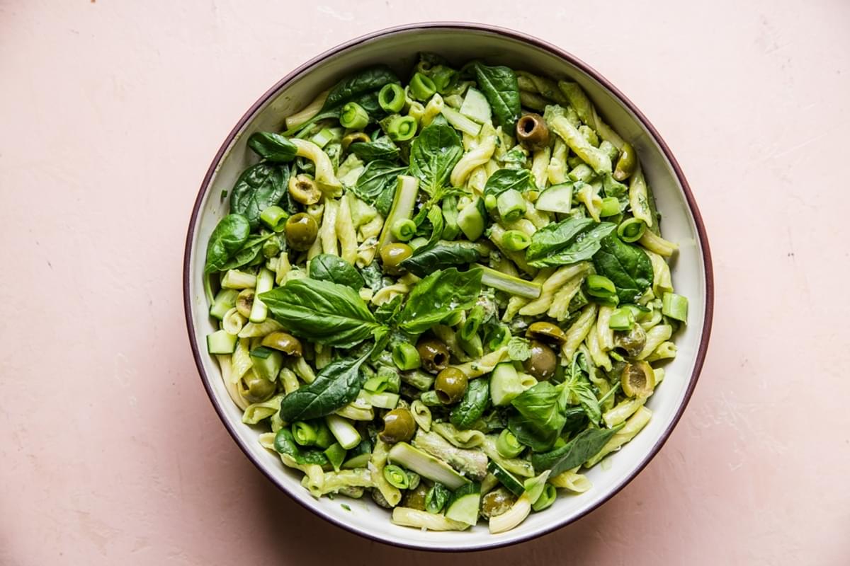 green goddess pasta salad in a serving bowl with olives, asparagus, spinach, basil and green onions