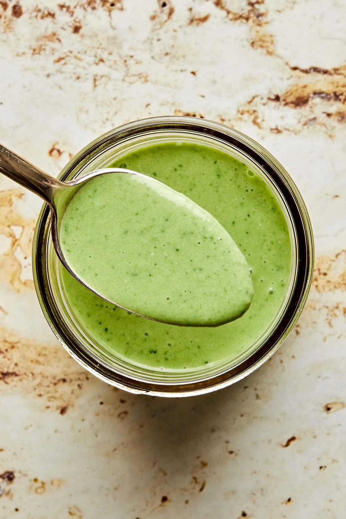 homemade green goddess dressing in a glass jar being scooped with a spoon