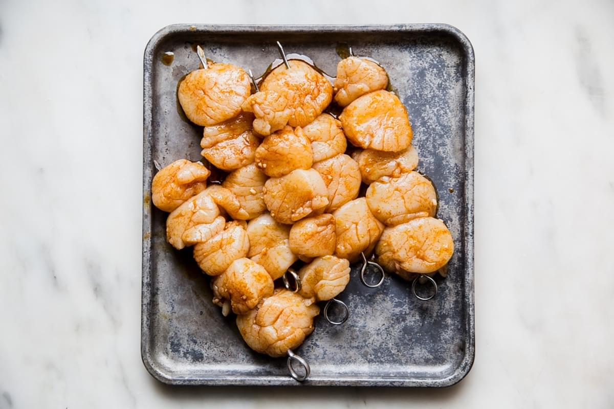 marinaded sea scallops on skewers on a baking sheet waiting to be grilled