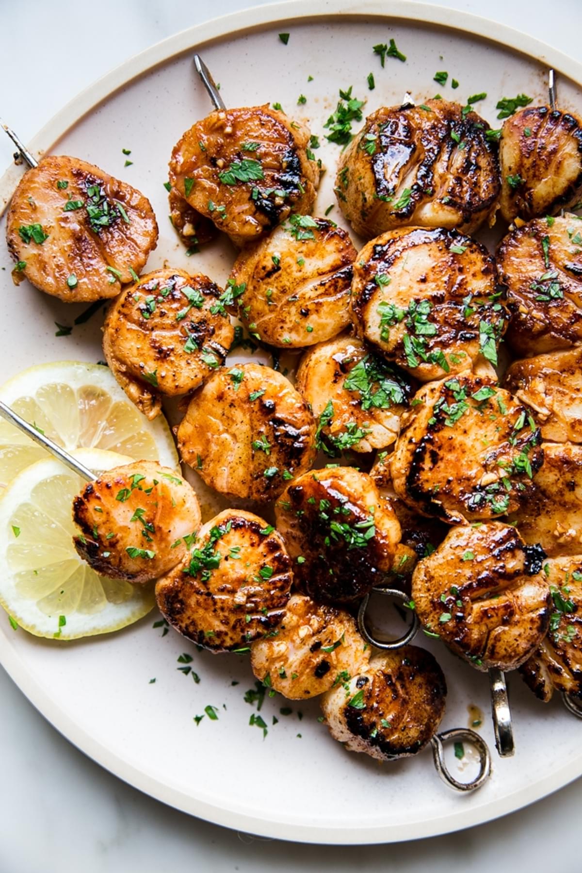 grilled scallops on skewers on a plate with lemon, and marinade
