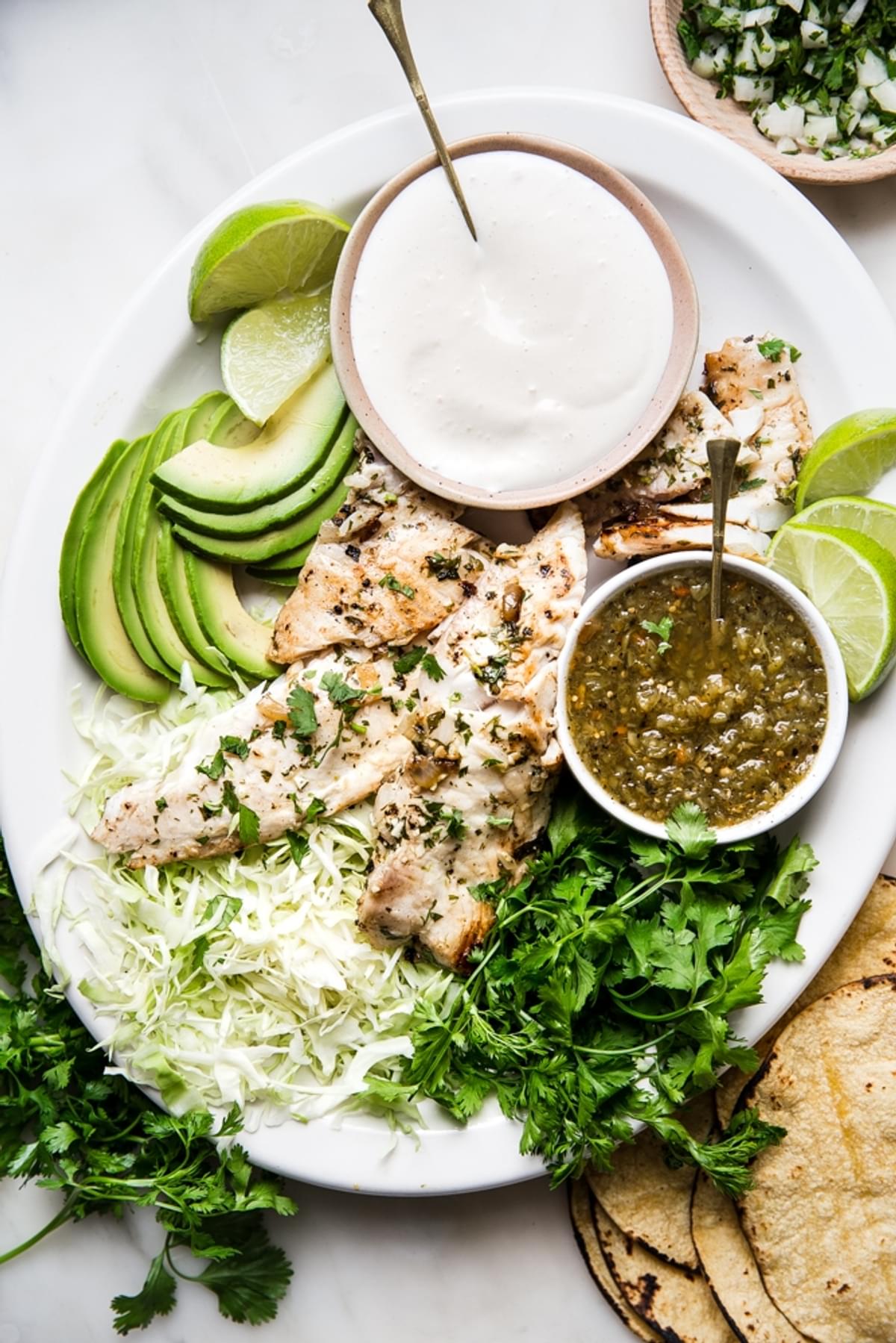 Grilled Tilapia on a plater with cilantro, salsa verde, cream, avocados and tortillas