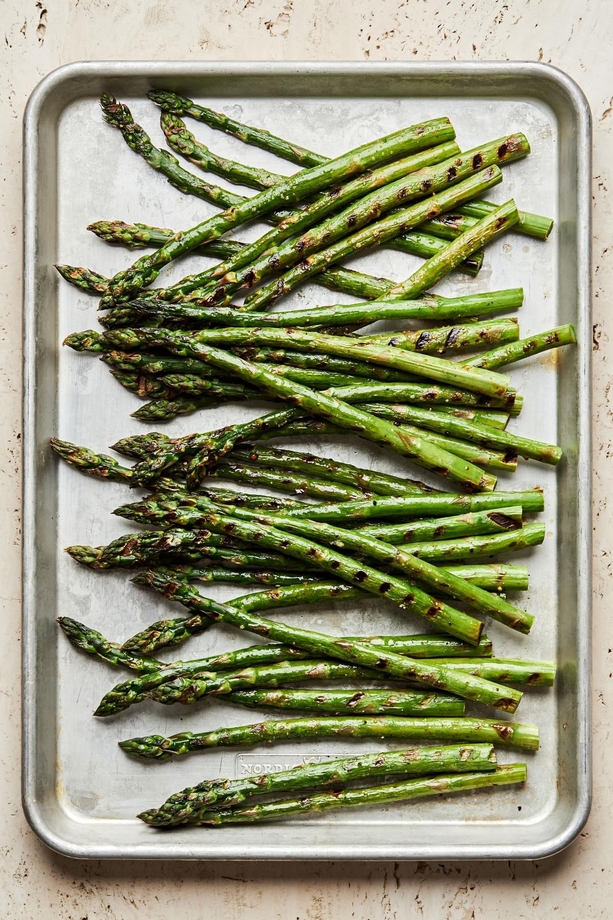 grilled asparagus seasoned with olive oil, salt & pepper resting on a baking sheet