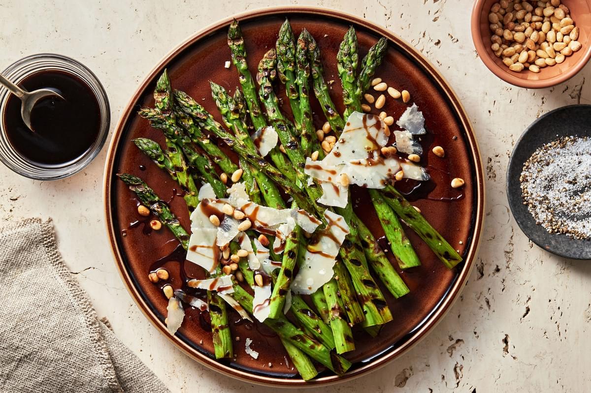 Grilled Asparagus with balsamic reduction sprinkled with parmesan cheese and pine nuts on a serving platter