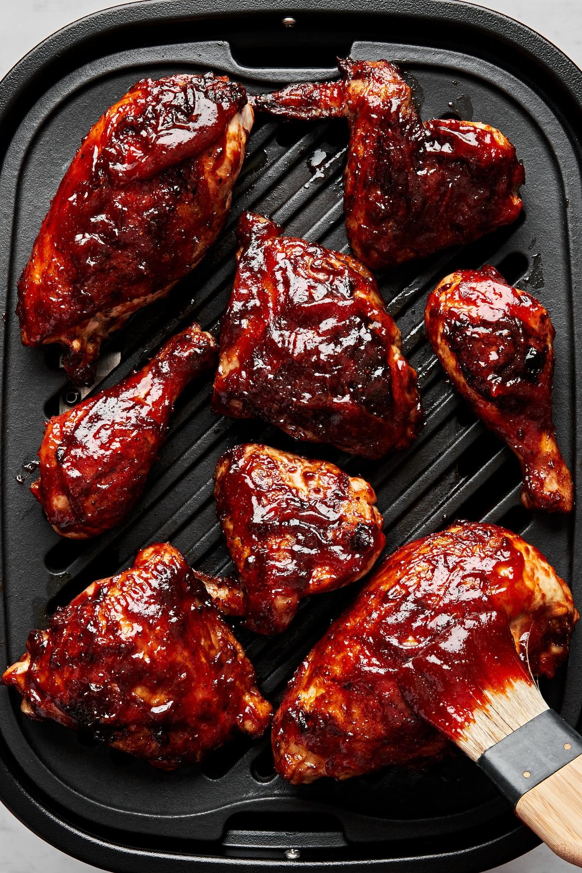 3 pounds chicken legs, thighs, wings and breasts being cooked on the grill and brushed with bbq sauce
