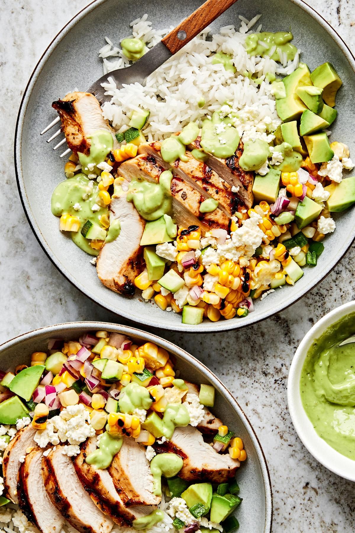 Grilled Chicken Bowl with corn and zucchini salad served on top of white rice in a bowl with a fork