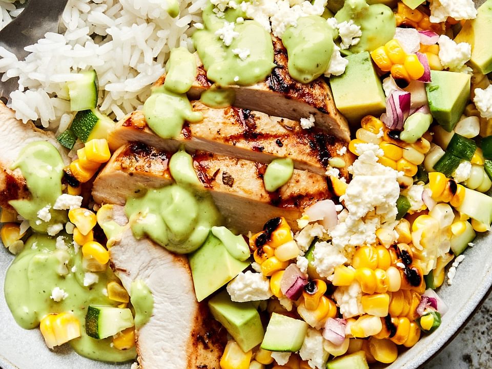 Grilled Chicken Bowl with corn and zucchini salad served on top of white rice in a bowl with a fork