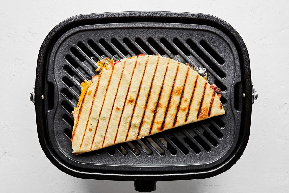 a chicken quesadilla being cooked on the grill filled with a cheese, onion, peppers, broccolini, cilantro and green onions