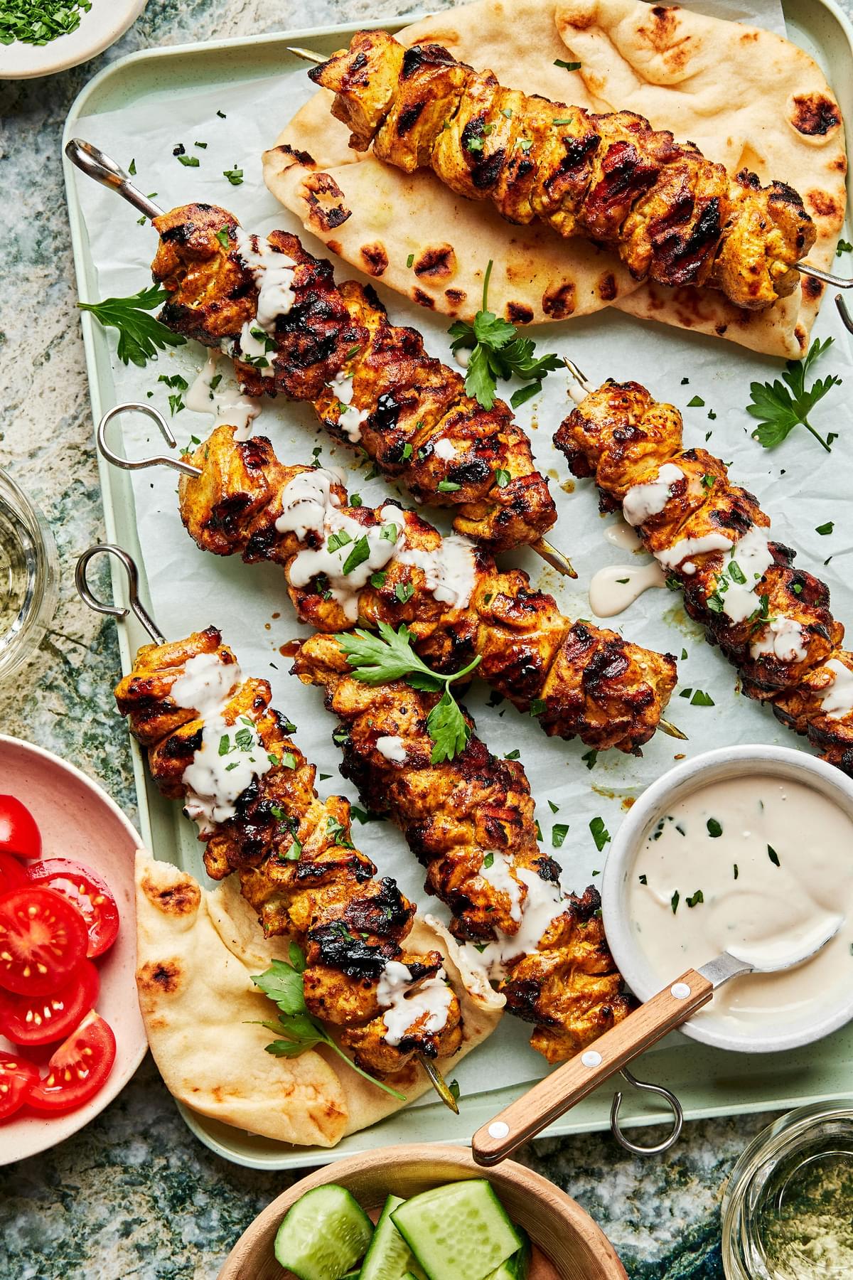 grilled chicken shawarma kebabs on a serving platter drizzled with tahini sauce being served with pita bread