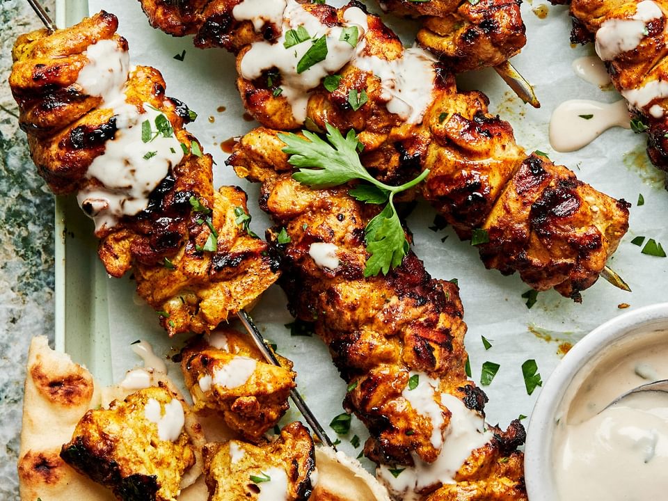 grilled chicken shawarma kebabs on a serving platter drizzled with tahini sauce served with pita bread