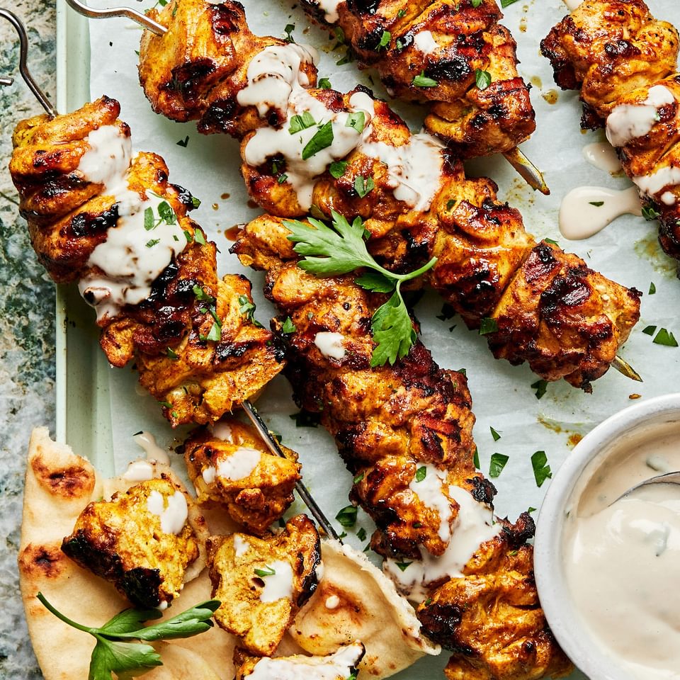 grilled chicken shawarma kebabs on a serving platter drizzled with tahini sauce served with pita bread