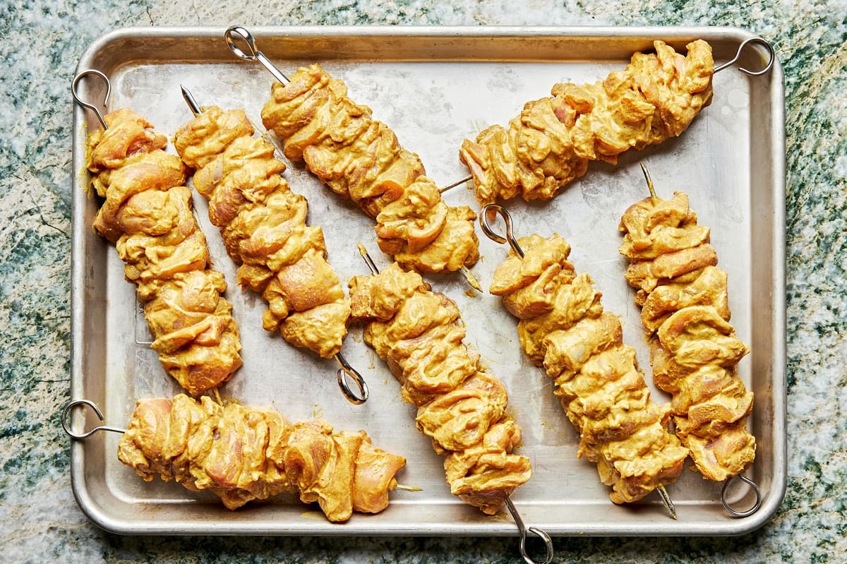 marinated chicken threaded on metal skewers on a baking sheet ready to be grilled