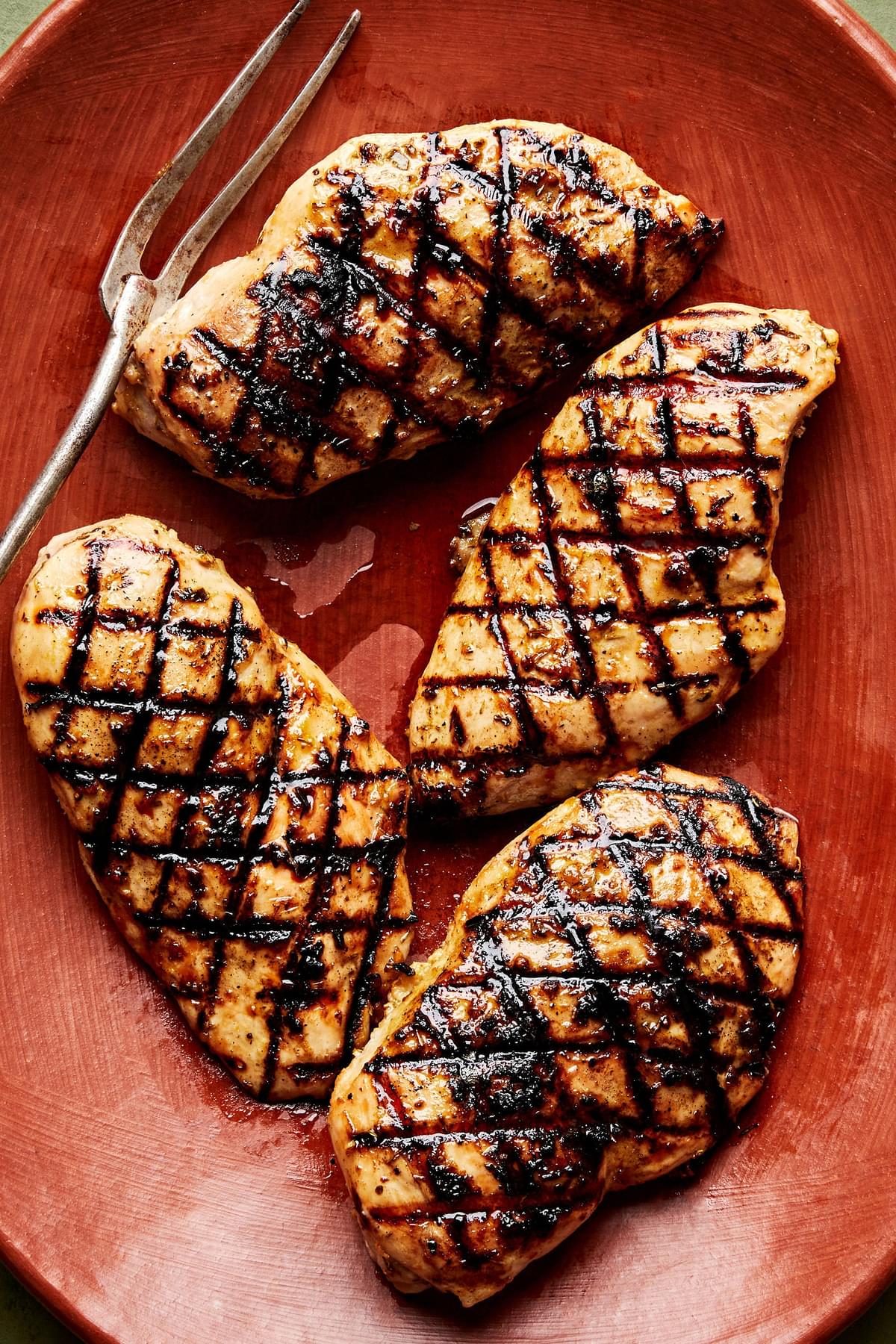 4 grilled chicken breasts on a serving platter with a serving fork