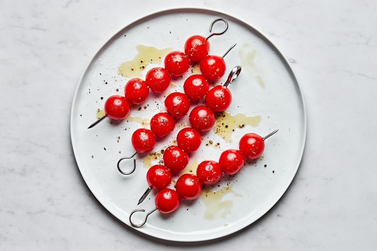 cherry tomatoes threaded on metal skewers drizzled with olive oil, salt and pepper