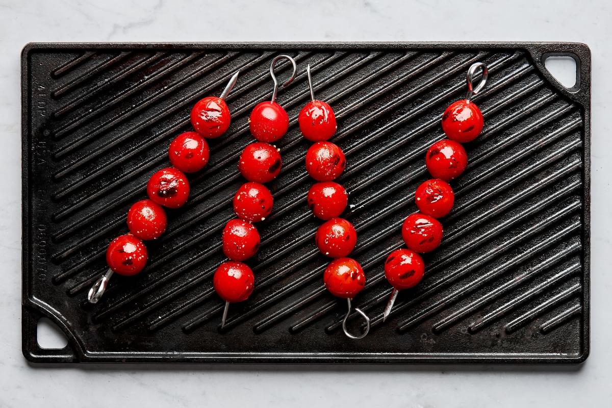 cherry tomatoes threaded on metal skewers drizzled with olive oil, salt and pepper being grilled on a cast iron grill pan