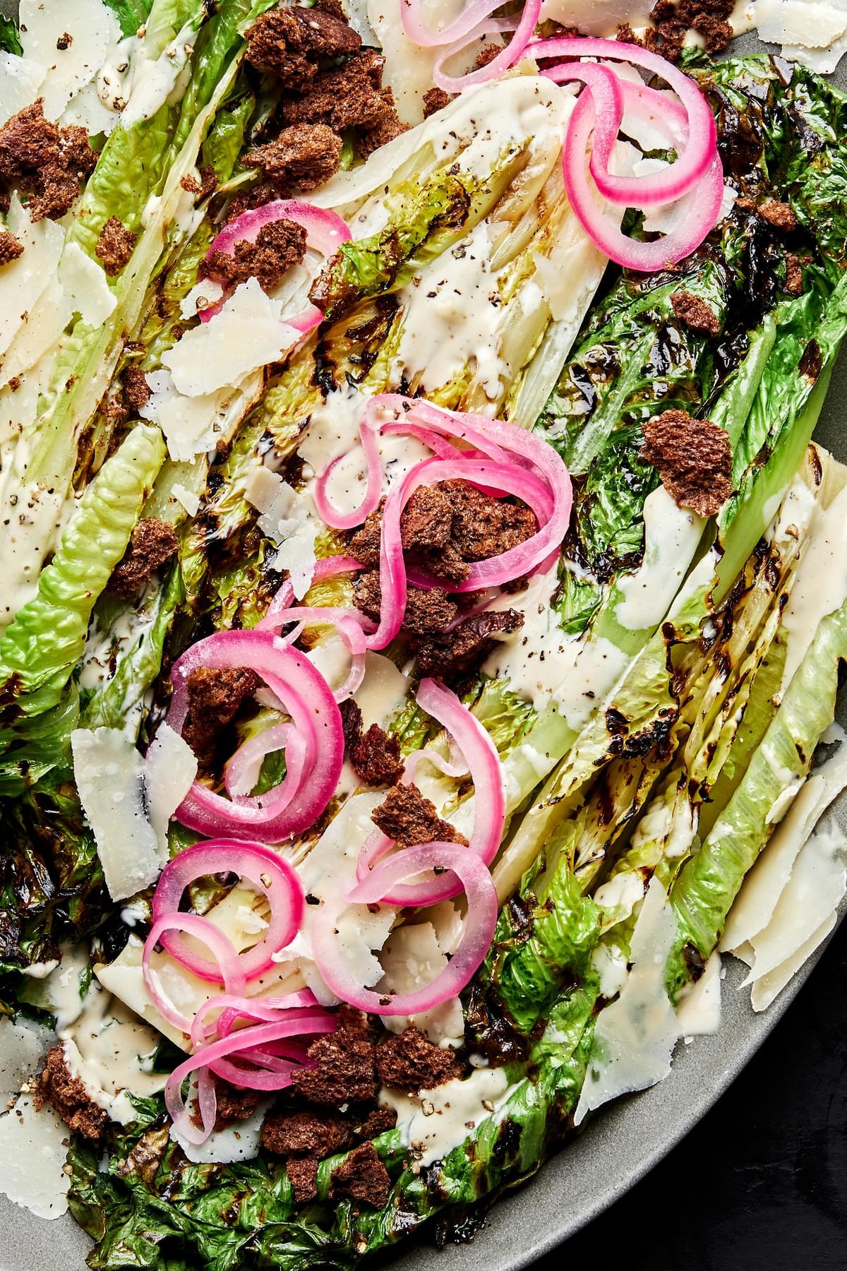 grilled romaine caesar salad with homemade dressing and topped with pickled onions and homemade breadcrumbs