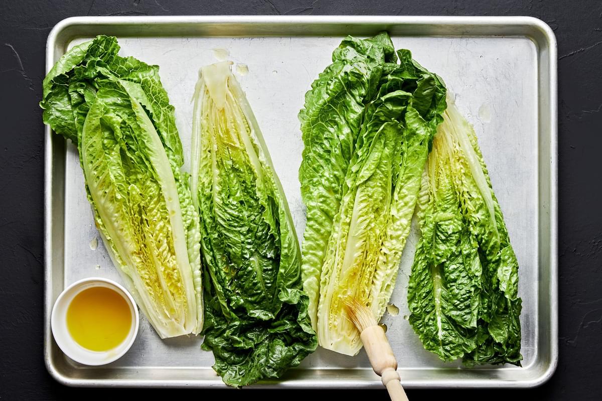Romaine lettuce heads brushed with olive oil on a baking sheet