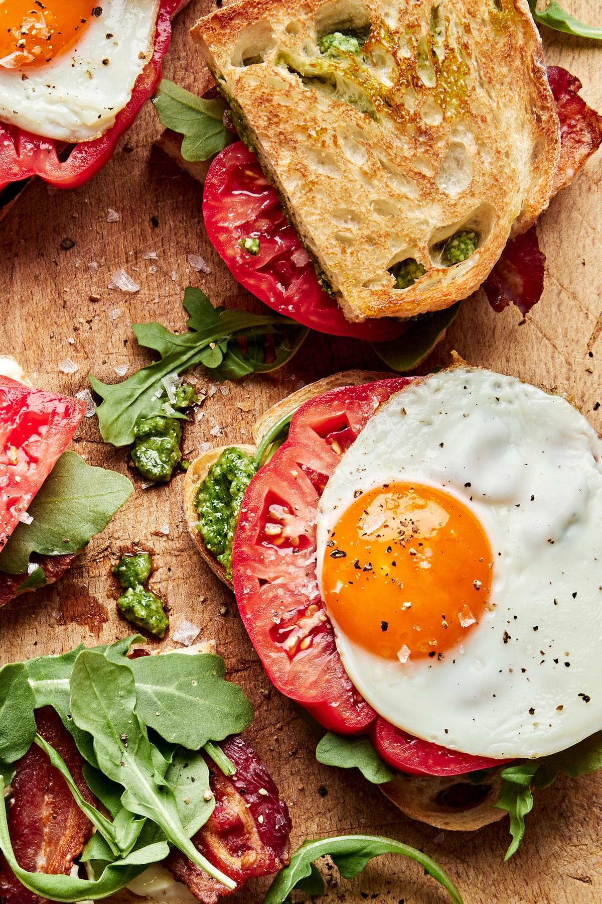 homemade heirloom tomato BLT sandwiches with pesto and fried eggs on a cutting board
