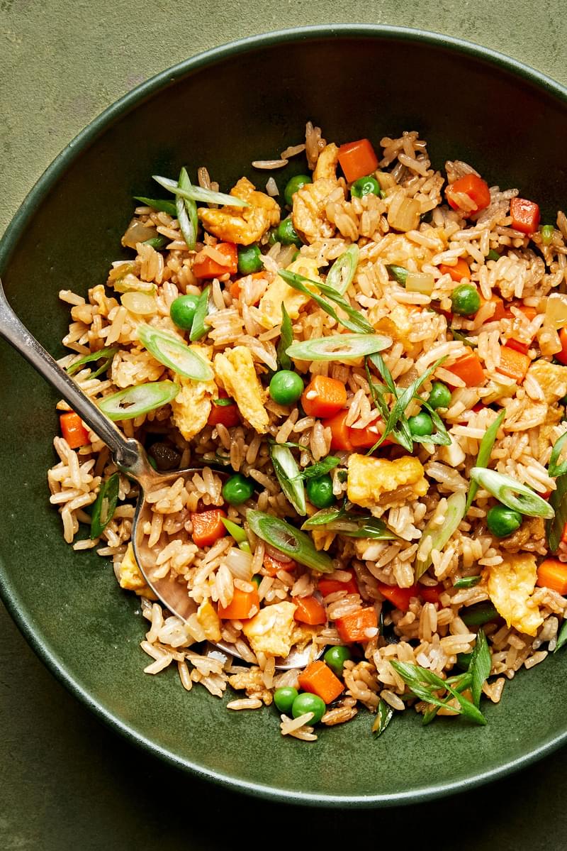 a bowl of homemade fried rice made with onion, eggs, carrots, garlic, peas, sesame oil and soy sauce topped with green onion