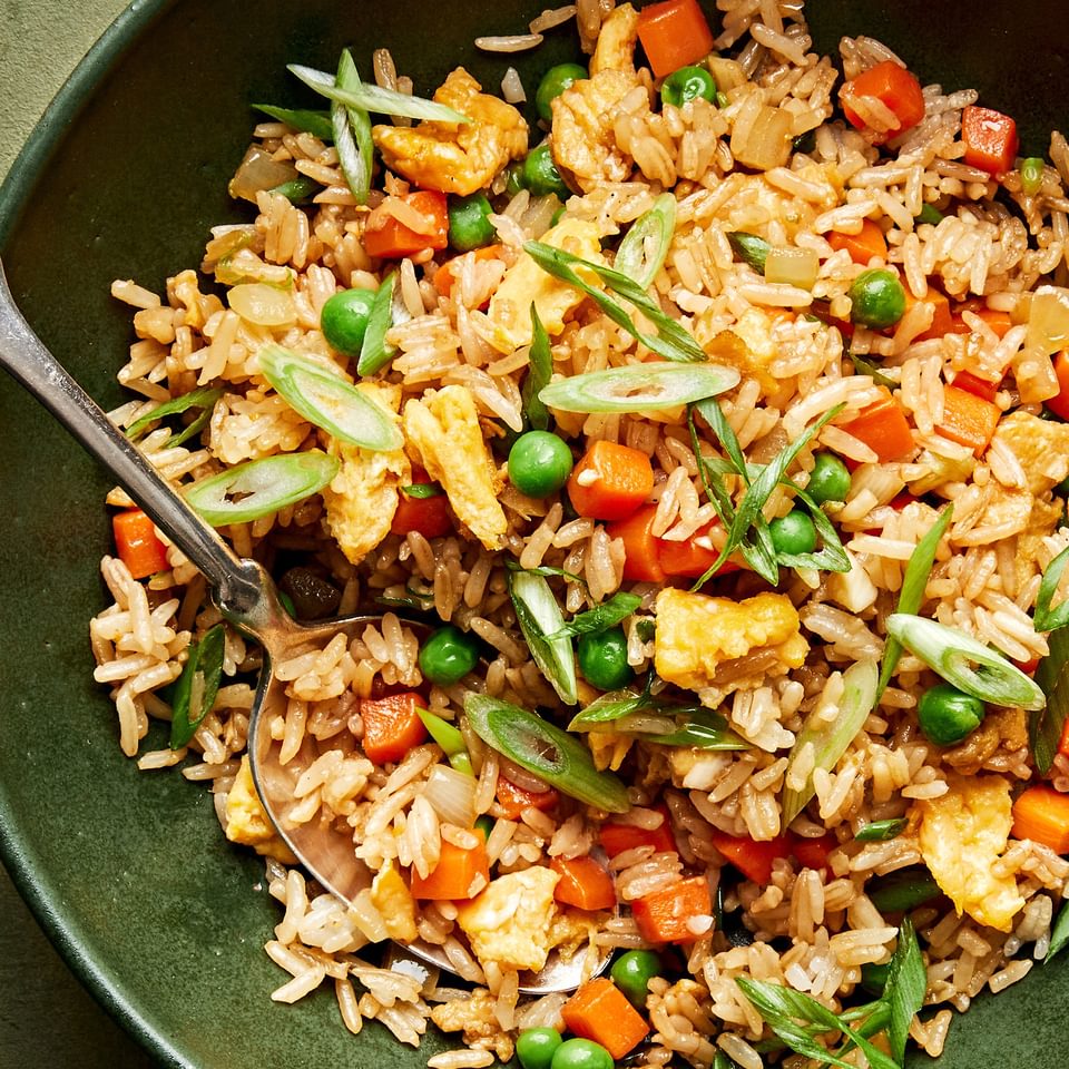 a bowl of homemade fried rice made with onion, eggs, carrots, garlic, peas, sesame oil and soy sauce topped with green onion