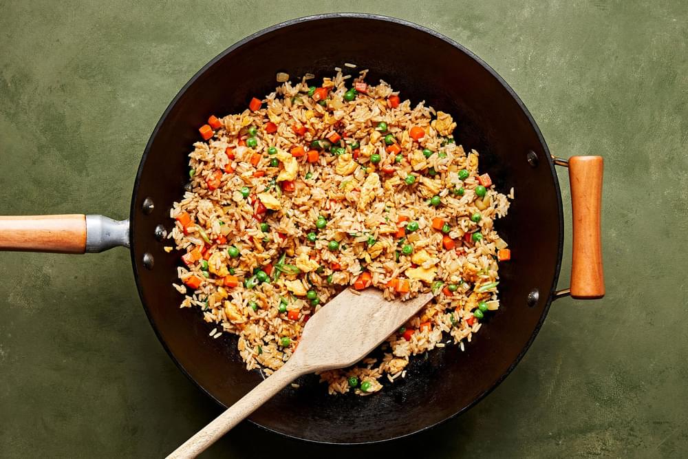 a wok of homemade fried rice made with onion, eggs, carrots, garlic, peas, sesame oil and soy sauce topped with green onion