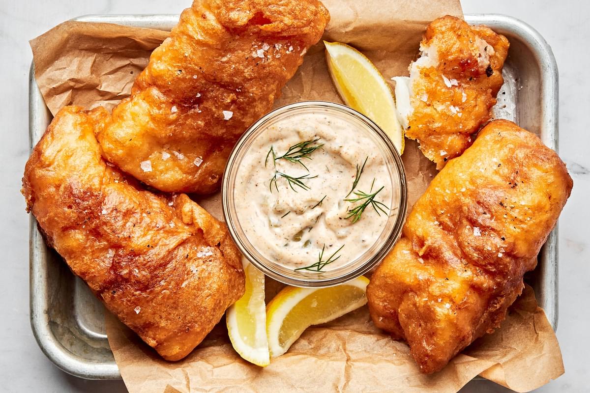 a bowl of homemade tartar sauce surrounded by beer battered fish and fries