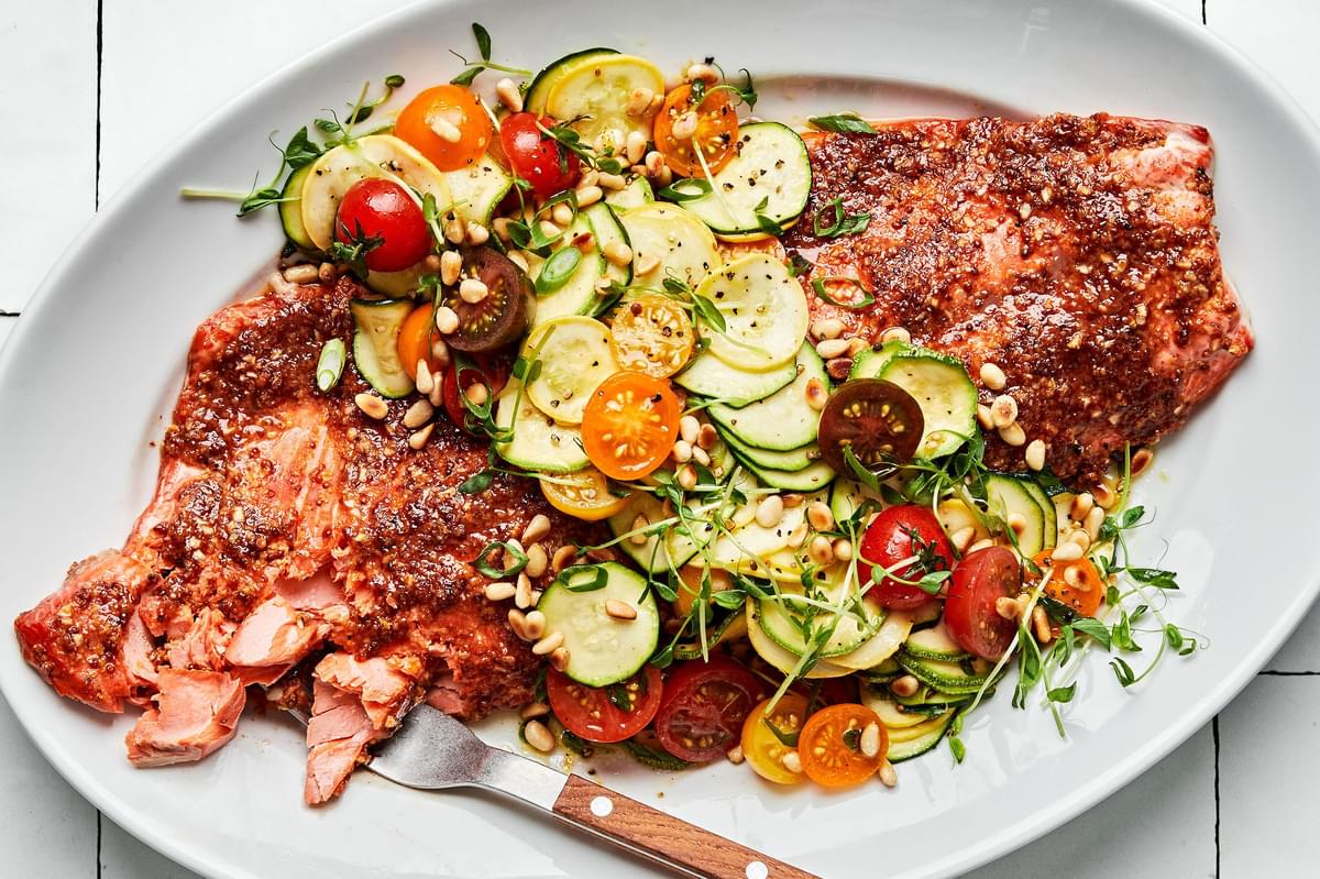 Honey Mustard Salmon with zucchini, squash, and tomato salad garnished with pine nuts on a serving platter
