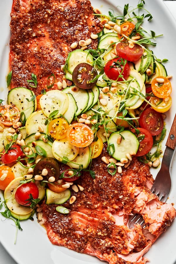 Honey Mustard Salmon with zucchini, squash and tomato Salad garnished with pine nuts on a serving platter