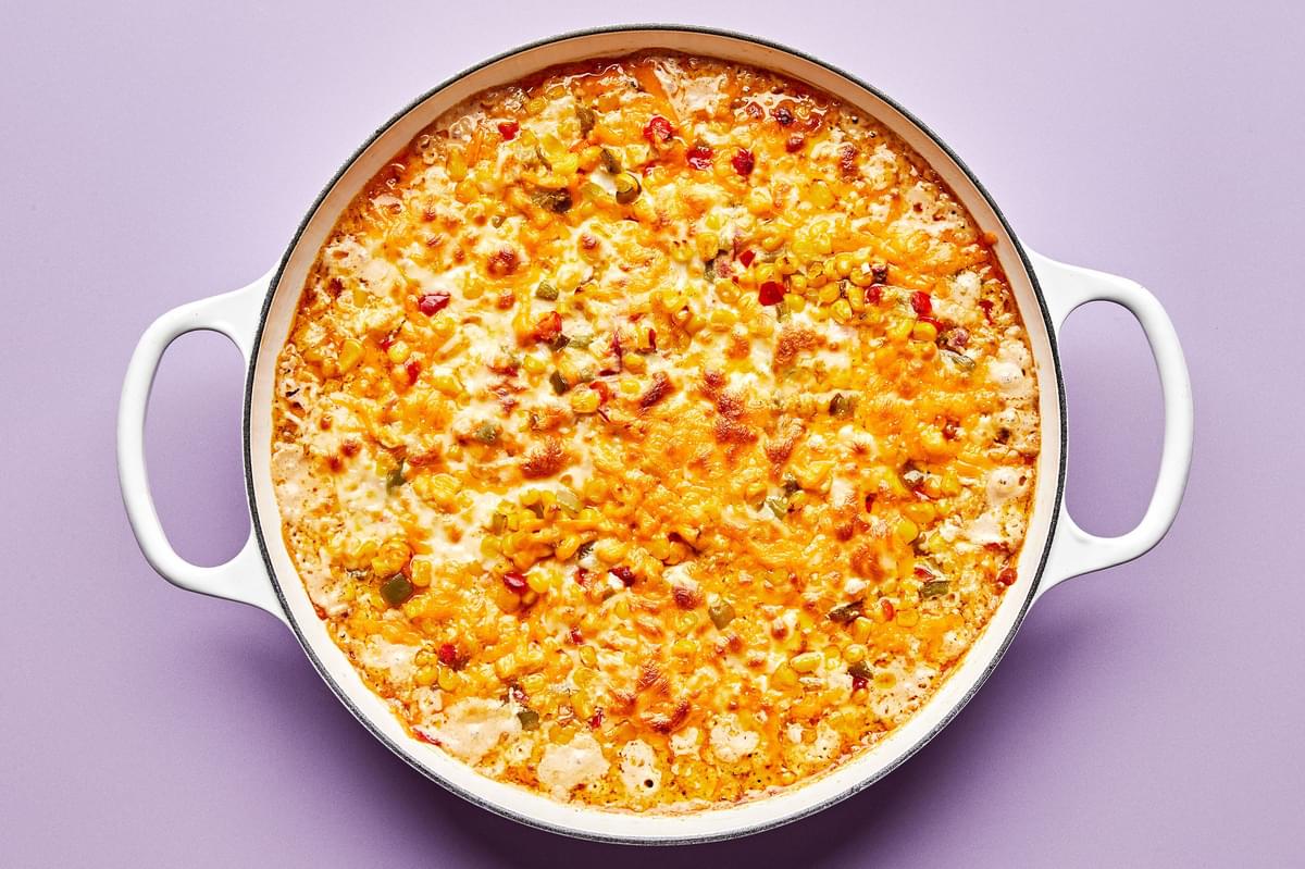 hot corn dip in a skillet made with cream cheese, sour cream, mayo, jalapeño, red onion, cheese & spices